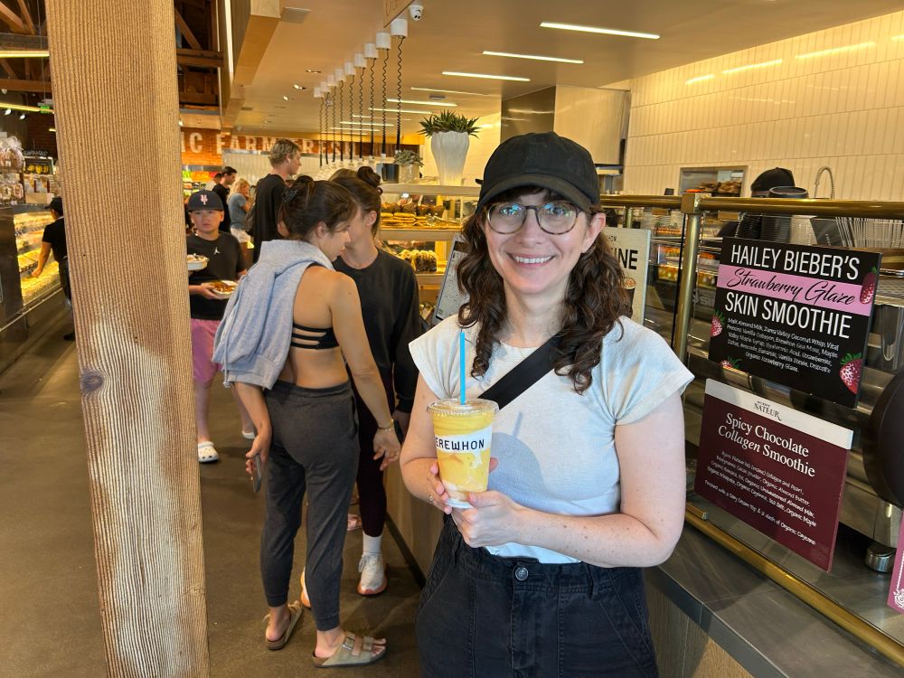 Me wearing a black baseball cap and white shirt, holding a mango smoothie 