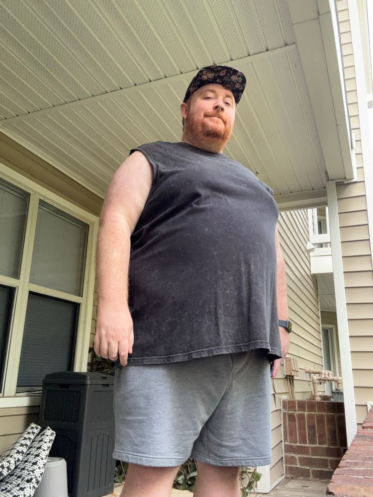 Cooper on his patio in a black sleeveless t-shirt, grey shorts, and a hat