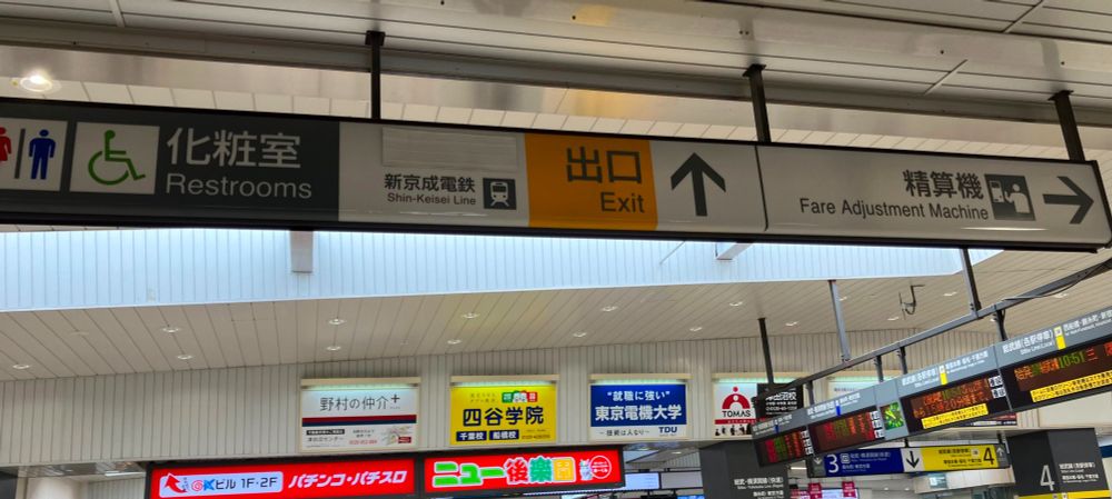 津田沼駅構内の案内表示。「出口」の文字の横、「新京成電鉄」の文字の上に、何かの文字が隠された痕跡。