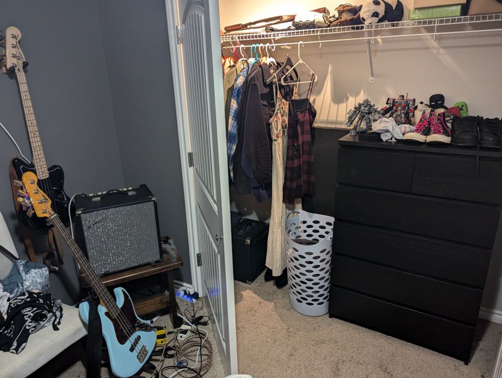 Bass guitars and amp on the left, opened closet on the right, with jackets and dresses on the left and dresser on the right, featuring transformers and shoes