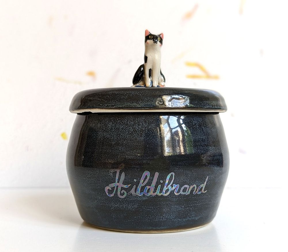 Cat urn for Hildibrand with a portrait figurine on top, it’s dark blue with the name handwritten in pearl luster 