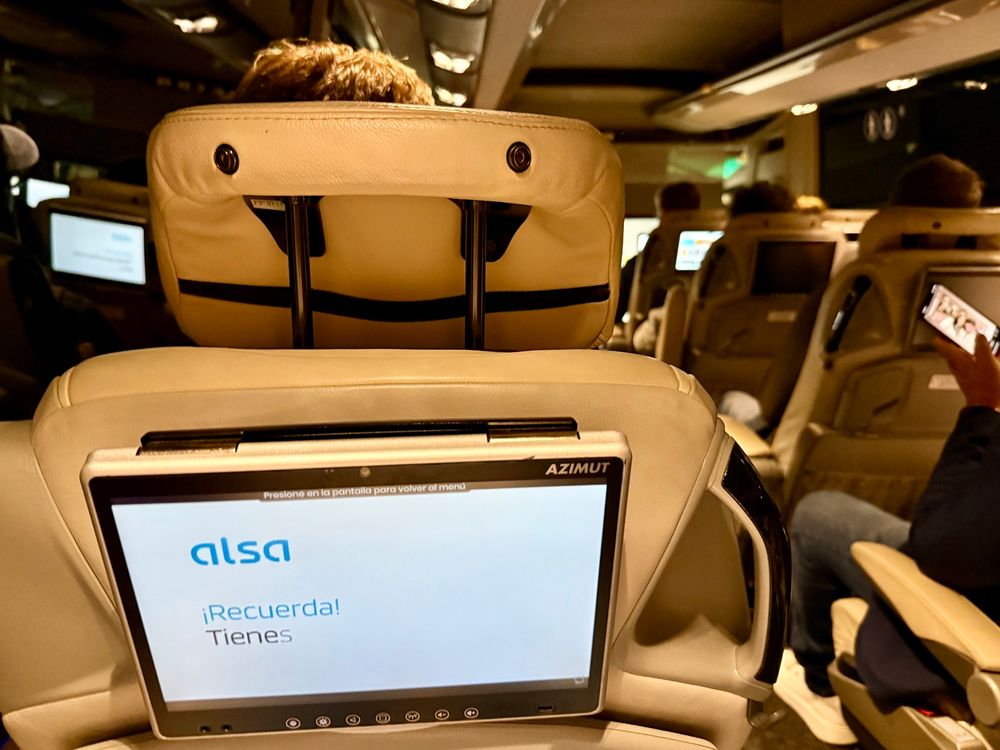 Innenansicht eines Alsa-Reisebusses mit bequemen Ledersitzen und individuellen Bildschirmen an den Rückenlehnen. Der Bildschirm zeigt eine Willkommensnachricht.