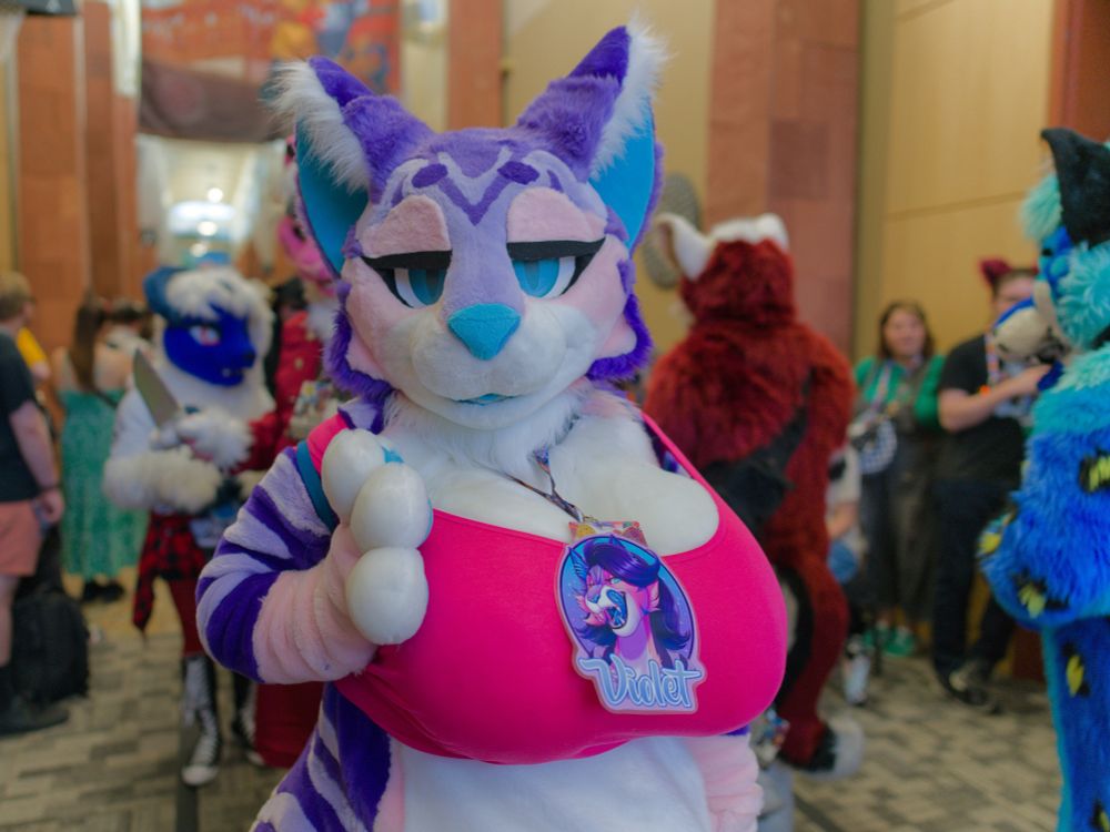 Fursuit parade with Violet wearing a pink top and gazing at the camera. 