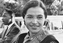 Black and white picture of Rosa Parks in a striped shirt wearing glasses with Martin Luther King Jr. in the background