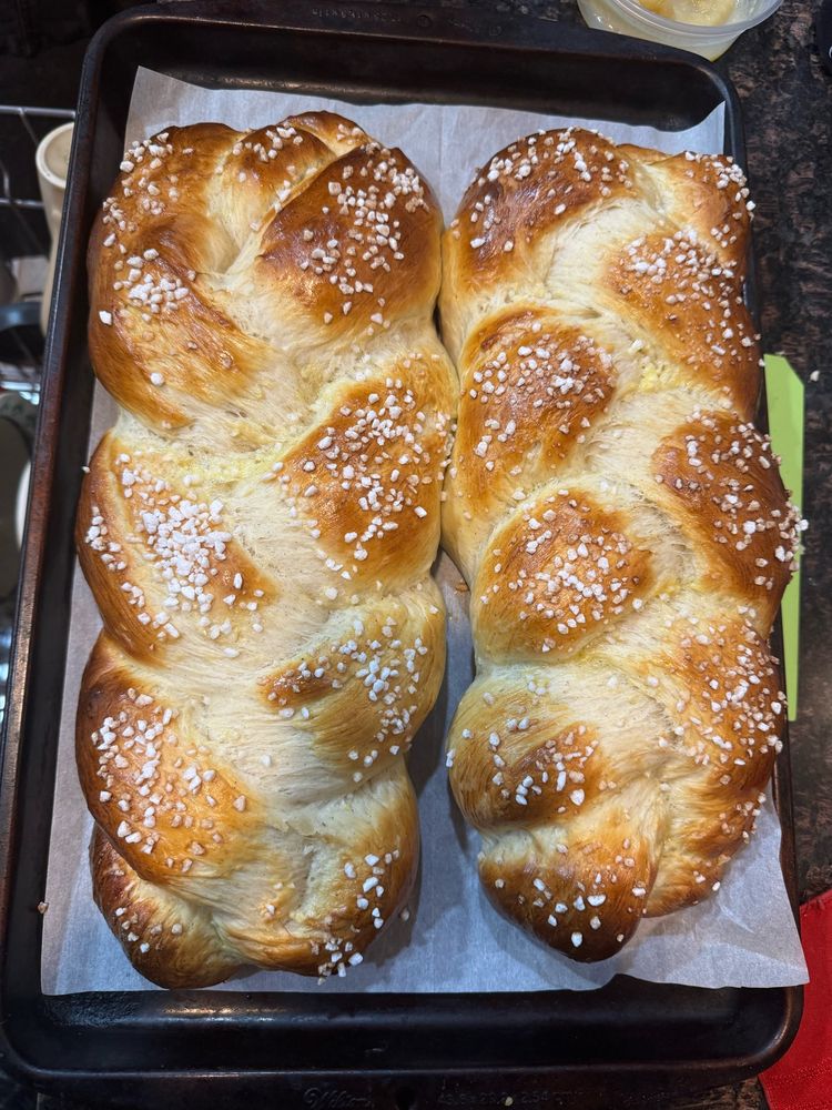 Two braided loaves sit on a parchment lined baking sheet. The braids rose a lot in the oven so the darker egg washed sections decorated with swedish pearl sugar contrast the white interior of the loaves.