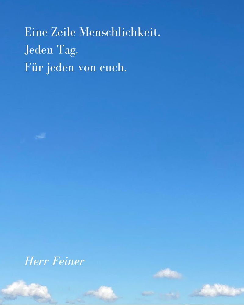 Blauer Himmel, am unteren Rand des Bildes einige kleine weisse Wolken. 
Vor dem Himmel der Text:_ 
Eine Zeile Menschlichkeit. 
Jeden Tag. 
Für jeden von euch. 