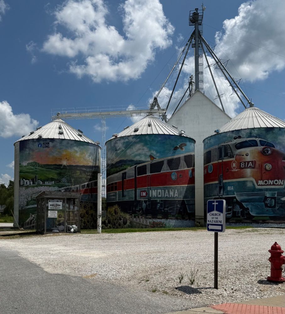 Three large grain bins painted with a large, vintage midcentury train depicted in three parts on each bin