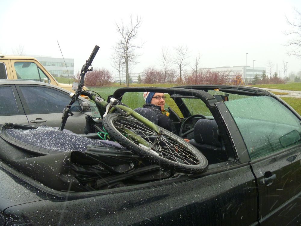 Photo of a black Volkswagen Cabriolet with the top down. Snow is falling lightly, and my green bike is in the back seat with Kent driving.