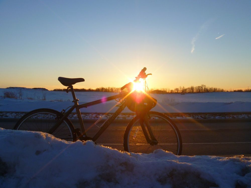 Photo of my green bike in front of a snowbank at sunset with the sun shining through the handlebars.