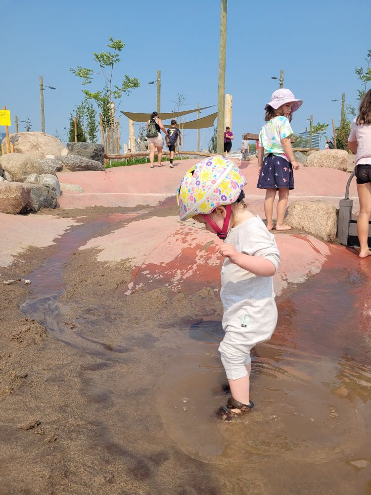 My daughter wearing a bike helmet and splashing in a water feature at the park