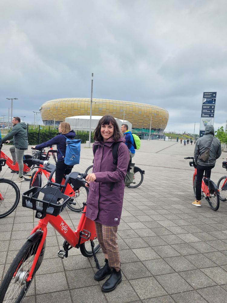 Me with a red Mevo bike share bike in front of the stadium in Gdansk, ready to depart on a group ride
