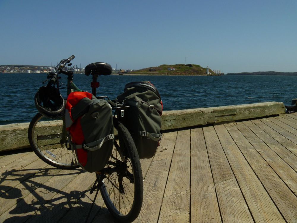 Photo of my green bike on the boardwalk in Halifax with full panniers and the ocean in the background.