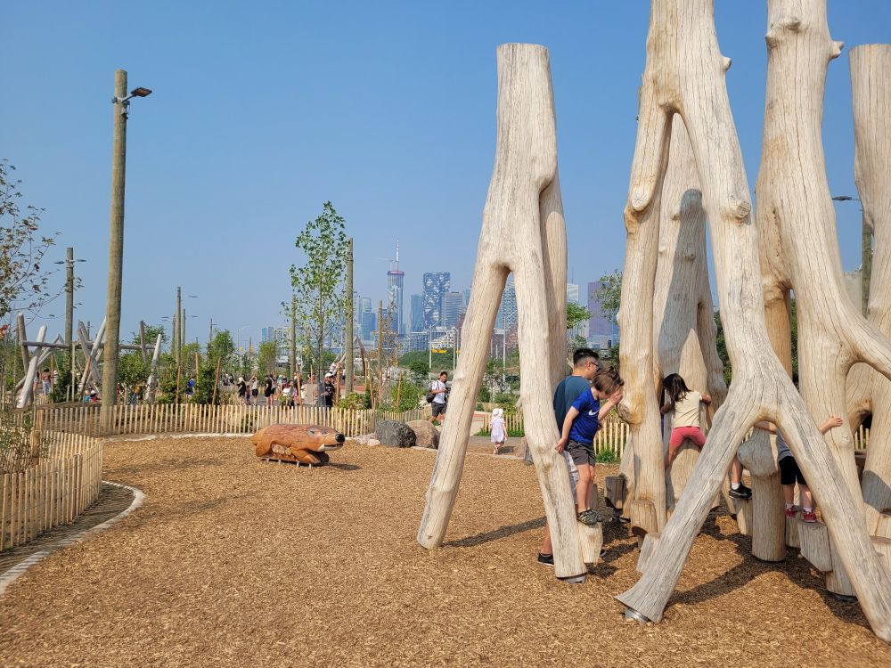 Kids playing on a wood log climber at Biidaasige Park 