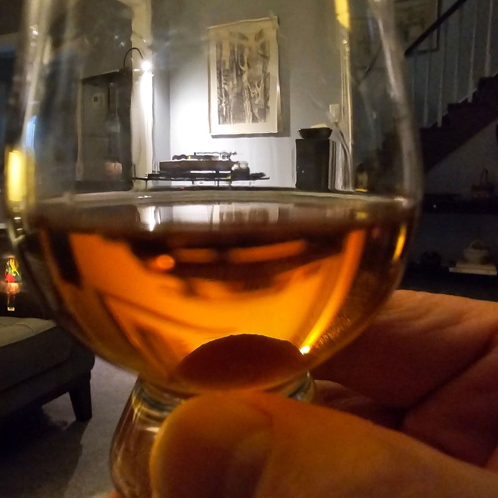 Extreme close up of bourbon in a glass. A turntable and part of a speaker can be seen in the background
