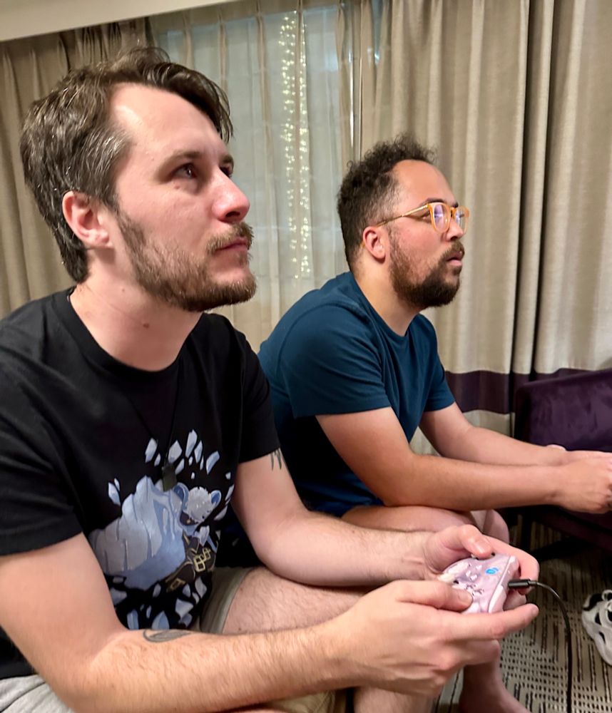 two men holding video game controllers and staring out of frame to the right, they both have stern expressions