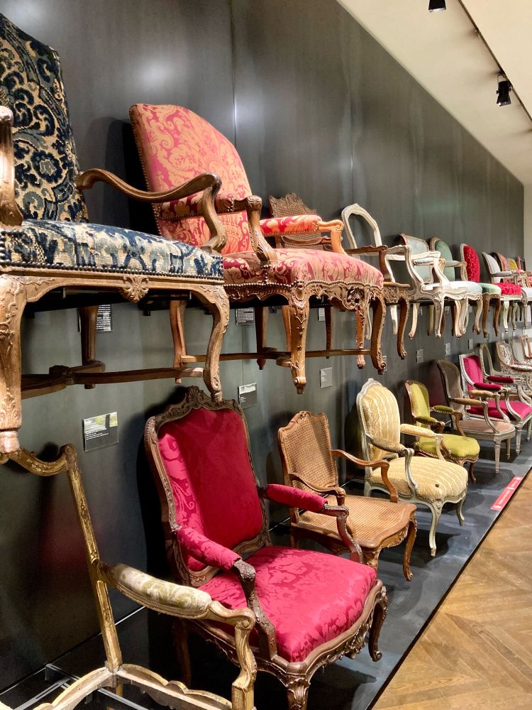 So wie heutzutage bei Ikea üblich, hängen in zwei Reihen an der Wand unterschiedlich gepolsterte Stühle aus dem 18. Jahrhundert