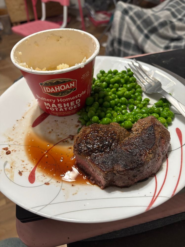 A partially eaten steak with peas and instant mashed potatoes.