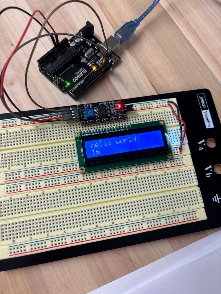 A breadboard with a 16x2 liquid crystal display that has the words “hello world!” printed above a count of the number of seconds the microcontroller has been active for