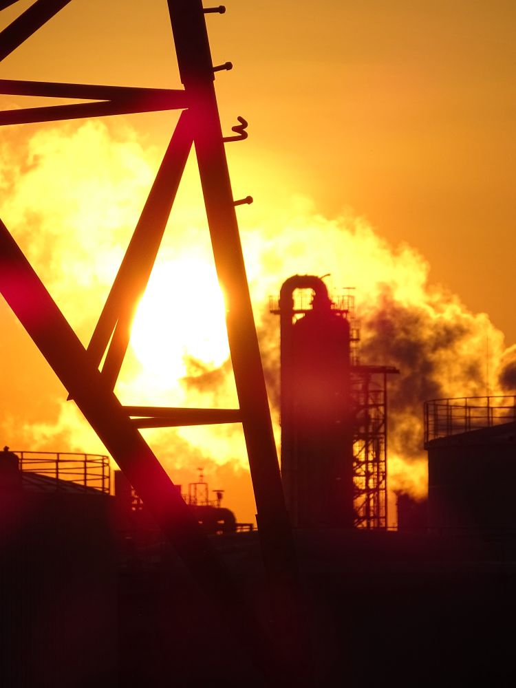 Sonnenuntergang im Industriegebiet. Mit rauchenden Schornsteinen und Eisengestellen.