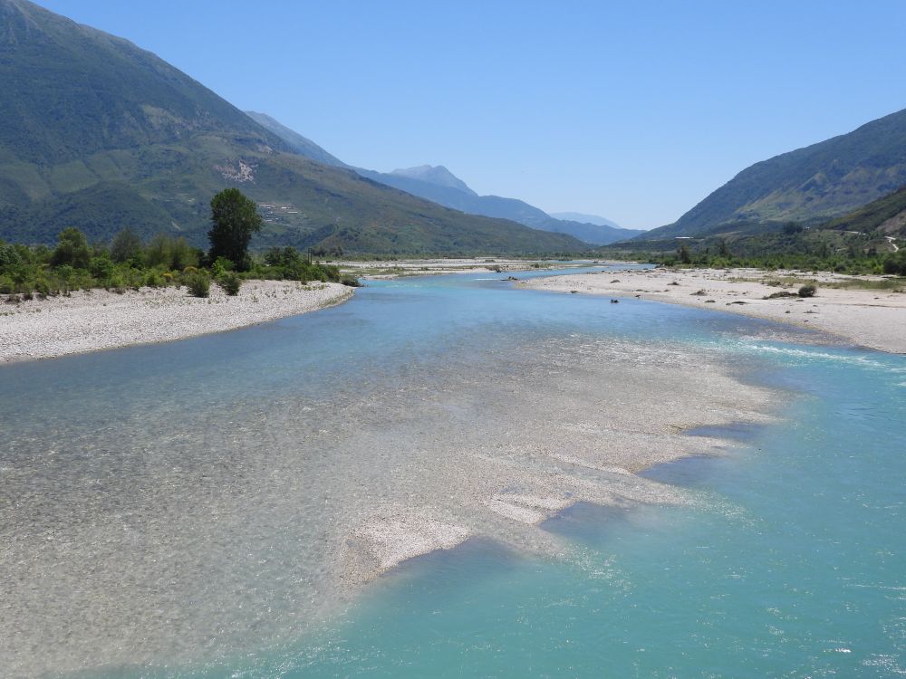 Kiesbank in der mitte eines unregulierten Flusses. Eisblaues und türkises wasser. Im hintergrund Hügelland und blauer Himmel.