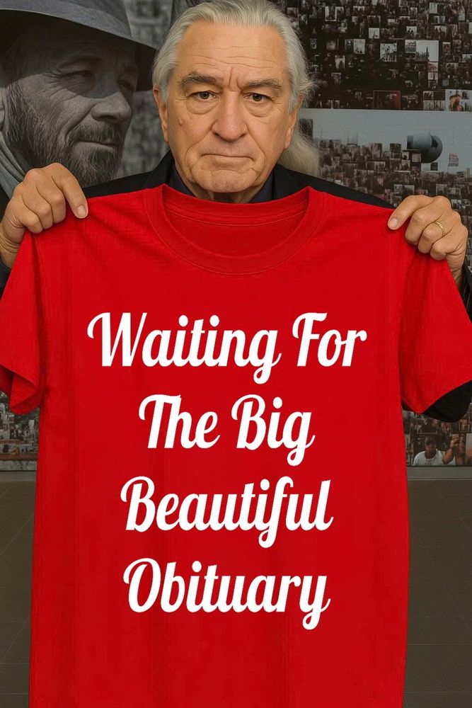 Man holding up a T shirt which says ' Waiting for the big beautiful obituary ' 
