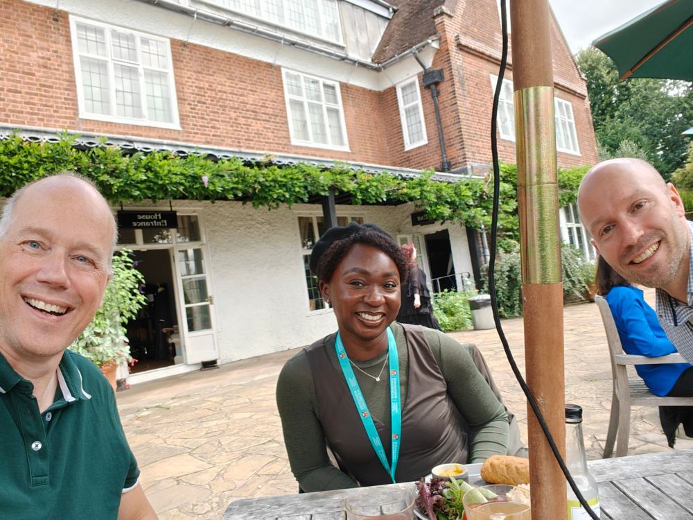 A selfie of three people, all smiling, having lunch in front of a red-brick building