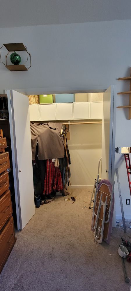 A closet with about a half-rack of clothing, white ikea boxes above with some cloth and cardboard boxes above that. 