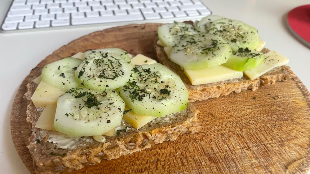 Zwei Brote mit Käse und Gurke belegt (kgb) auf einem Holzbrett