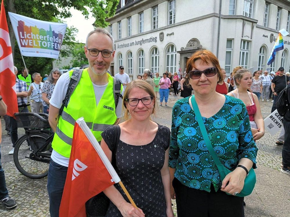 Mitglieder der Linken Steglitz-Zehlendorf auf dem Vorplatz des S-Bahnhofs Lichterfelde Ost am Jungfernstieg. Dahinter Banner von Lichterfelde weltoffen, Omas gegen Rechts und zahlreiche Demonstrierende.