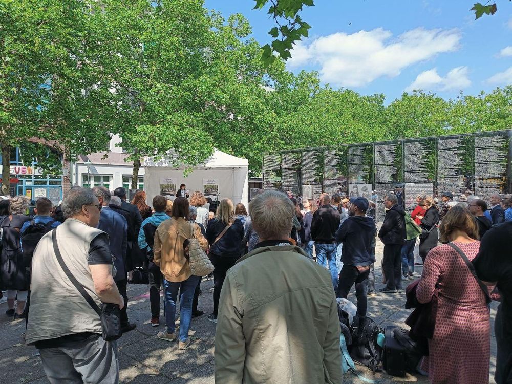 Ein weißes Pavillonzelt mit Rednerin und Plakaten neben der Spiegelwand auf dem Hermann-Ehlers-Platz. Bei sonnigem Wetter stehen zahlreiche Zuschauer*innen verschiedenen Alters davor.