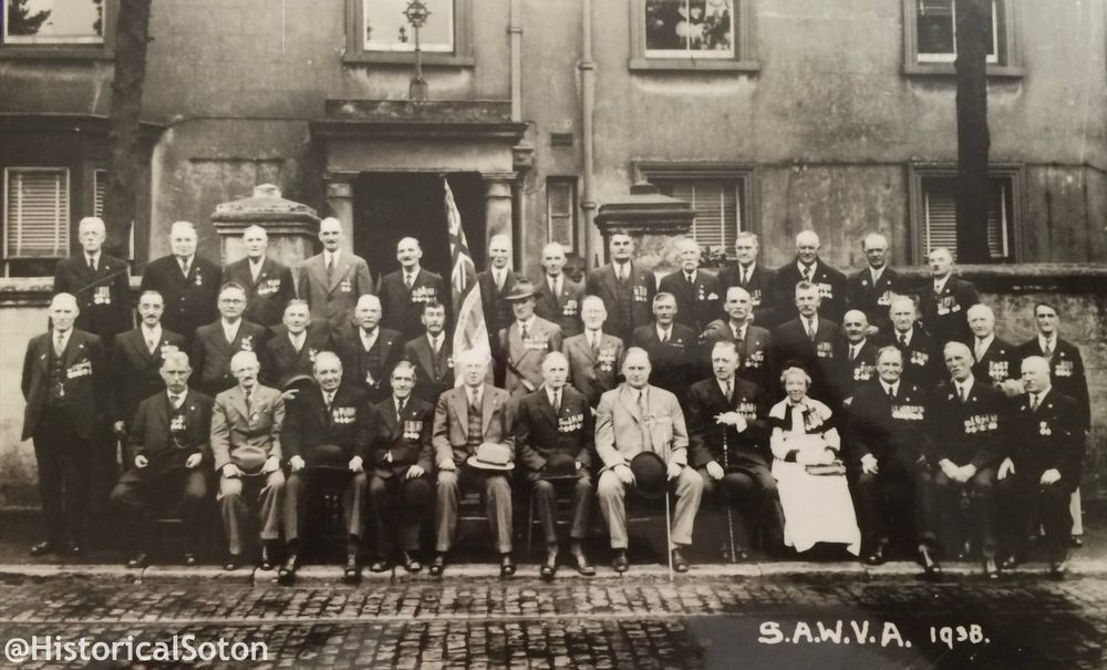 Group photo of members of the association. One lone woman, the rest men in suits. All wear medals. 