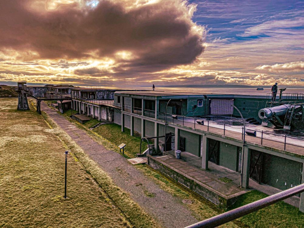 a highly processed photo of Fort Casey on Whidbey Island, Washington. The processing looks fairly unnatural, and emphasis is placed on the textures of the clouds, grass, and fort structure. There is a cannon visible and a couple unidentified figures on top of the fort.