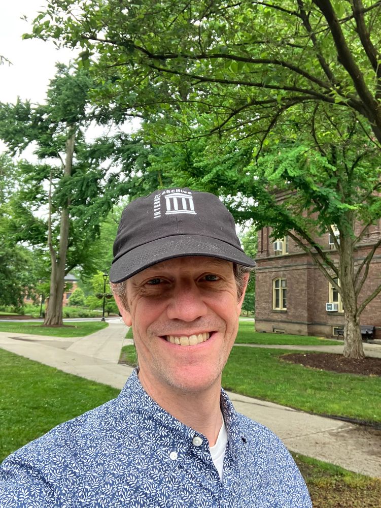 A man wearing a "Internet Archive" baseball cap against a leafy collegiate background
