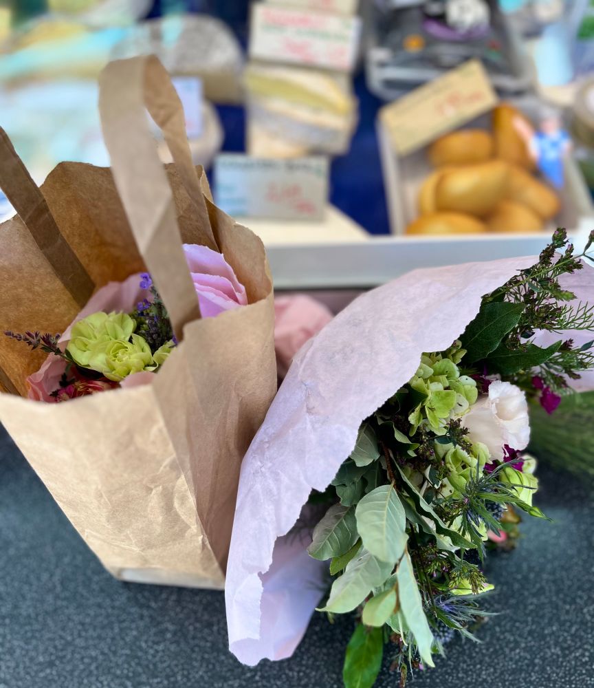 ein Blumenstrauß und eine Tüte mit einem weiteren Blumenstrauß vor der Käsetheke