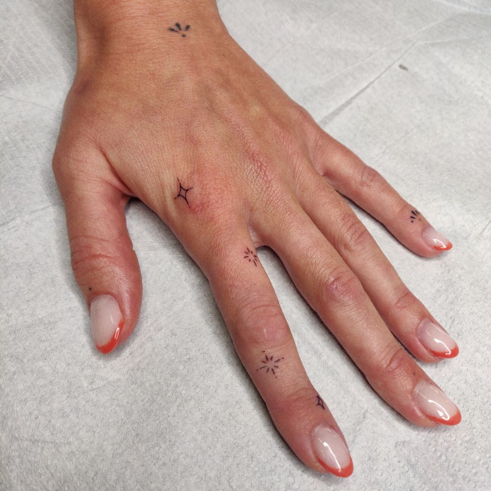 Photo of a hand with small sparkle tattoos on the pointer finger. 