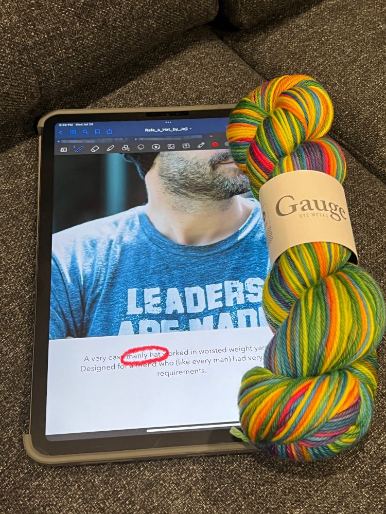 An iPad showing a knitting pattern described as a "manly hat," along with a hank of brightly-colored self-striping yarn by Gauge Dye Works.