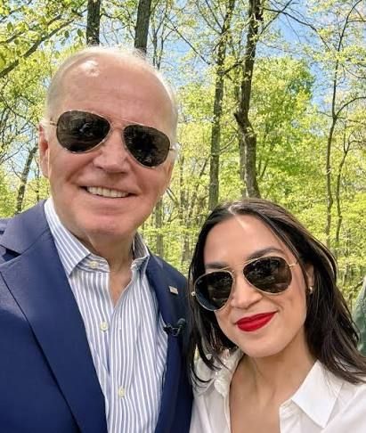 AOC and Biden smiling and wearing sunglasses as AOC campaigns for Biden while he committed a genocide 