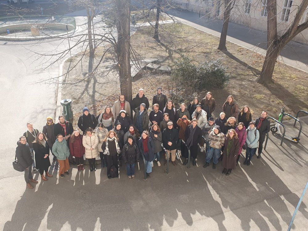 Group picture of participants in the 2025 Winter School of Finno-Ugric Studies, standing in an ice-cold but sunny courtyard, some participants wearing winter jackets, hats, and gloves, some participants wearing just a sweater.