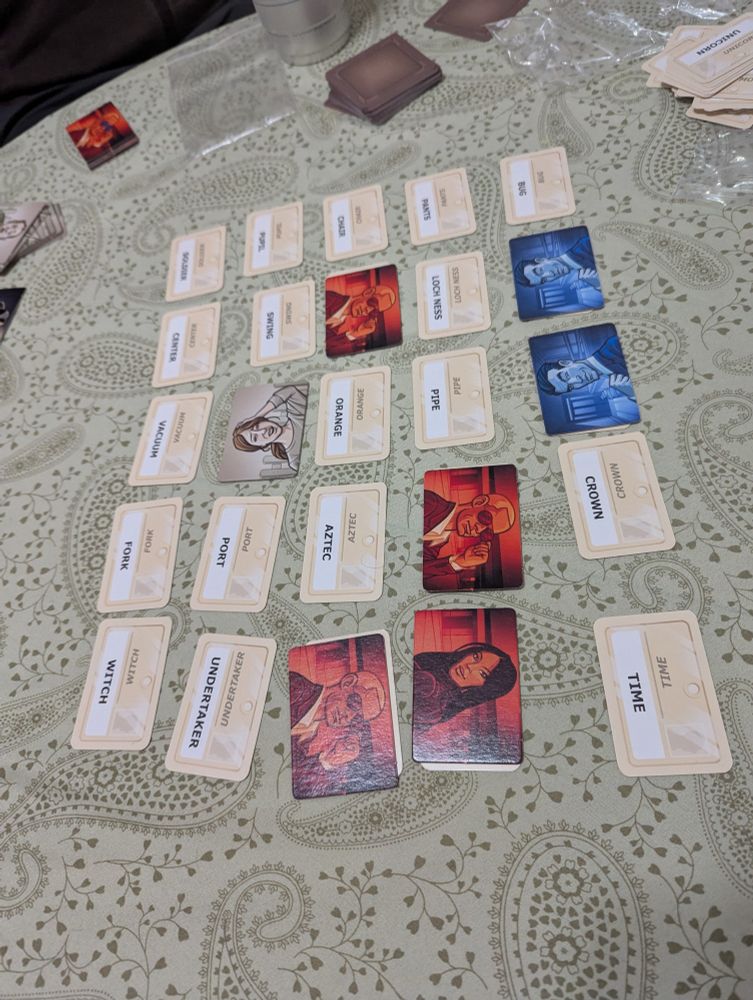 The game Codenames laid out on a table.  Red has discovered four agents, blue has three.