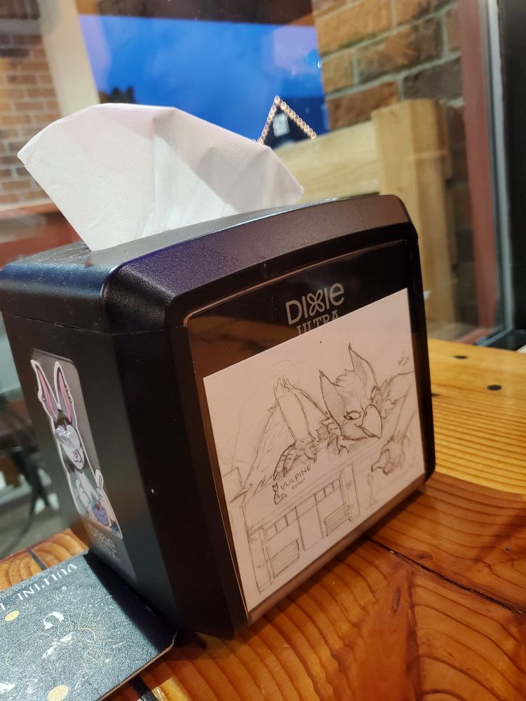 Picture of a napkin holder at Vulpine Taproom, with a sketch by me of a giant Ruby lounging atop the strip mall over Vulpine