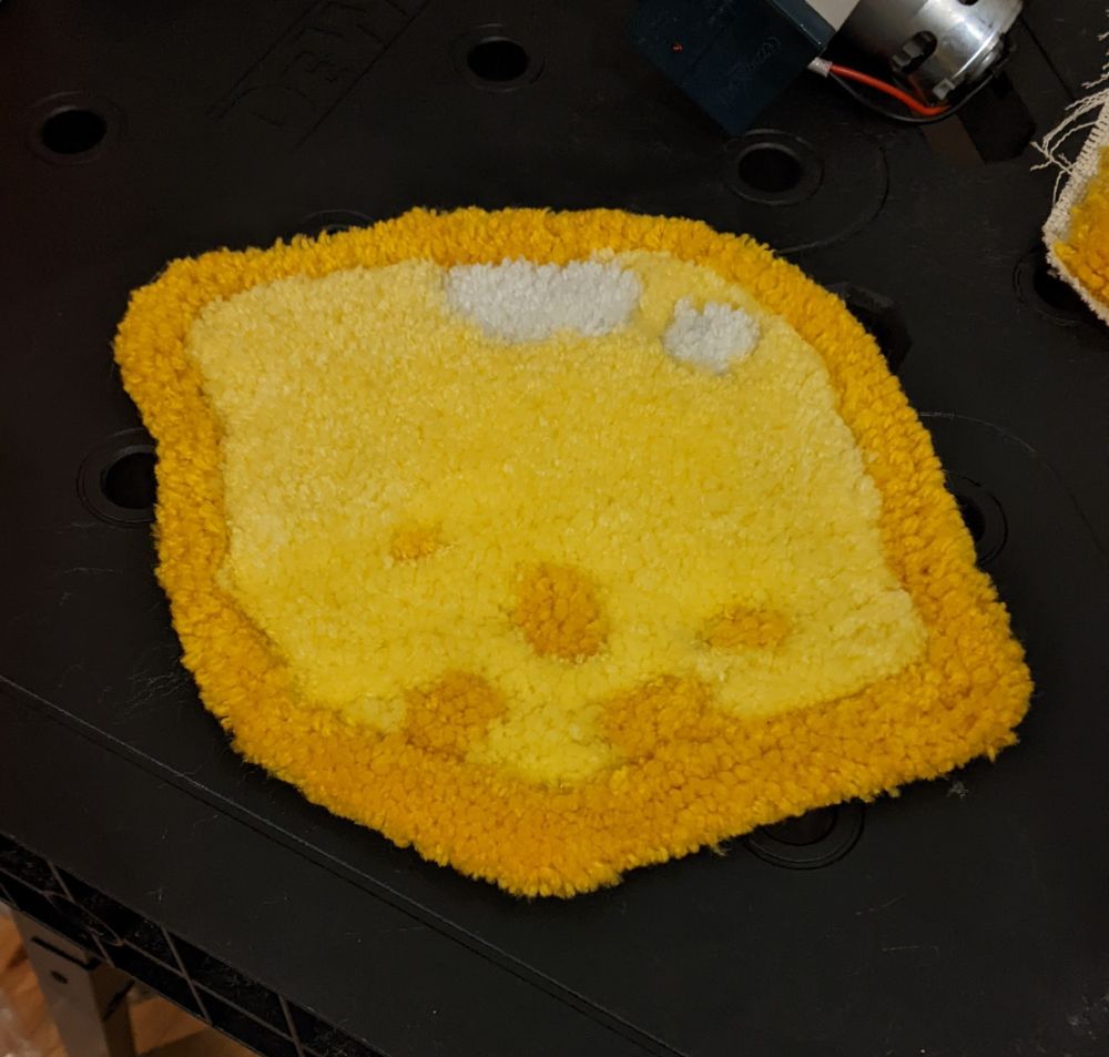 A tufted rug of a lemon that is yellow, has a gold border, and spots to give the impression of the texture of lemon skin. It's less than a foot long.