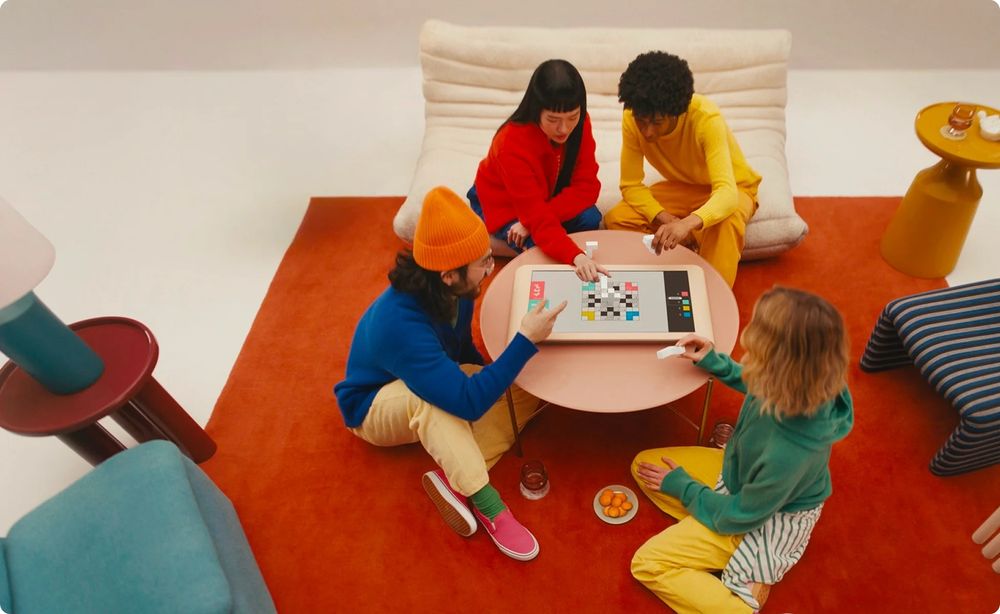 A group of trendy adults in sat amongst some bright interior design in even brighter clothing playing with their Board (which looks like a massive iPad)