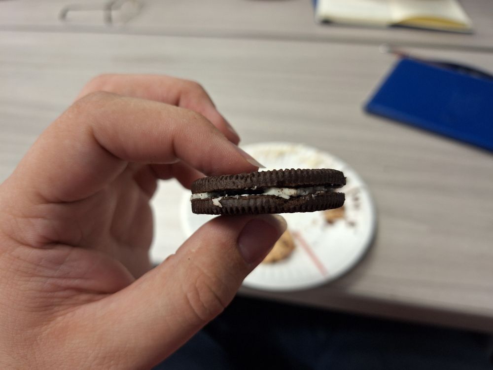 A side view of an oreo cookie with most of its cream missing. A portion of the center is vacant allowing a view of the background through it.