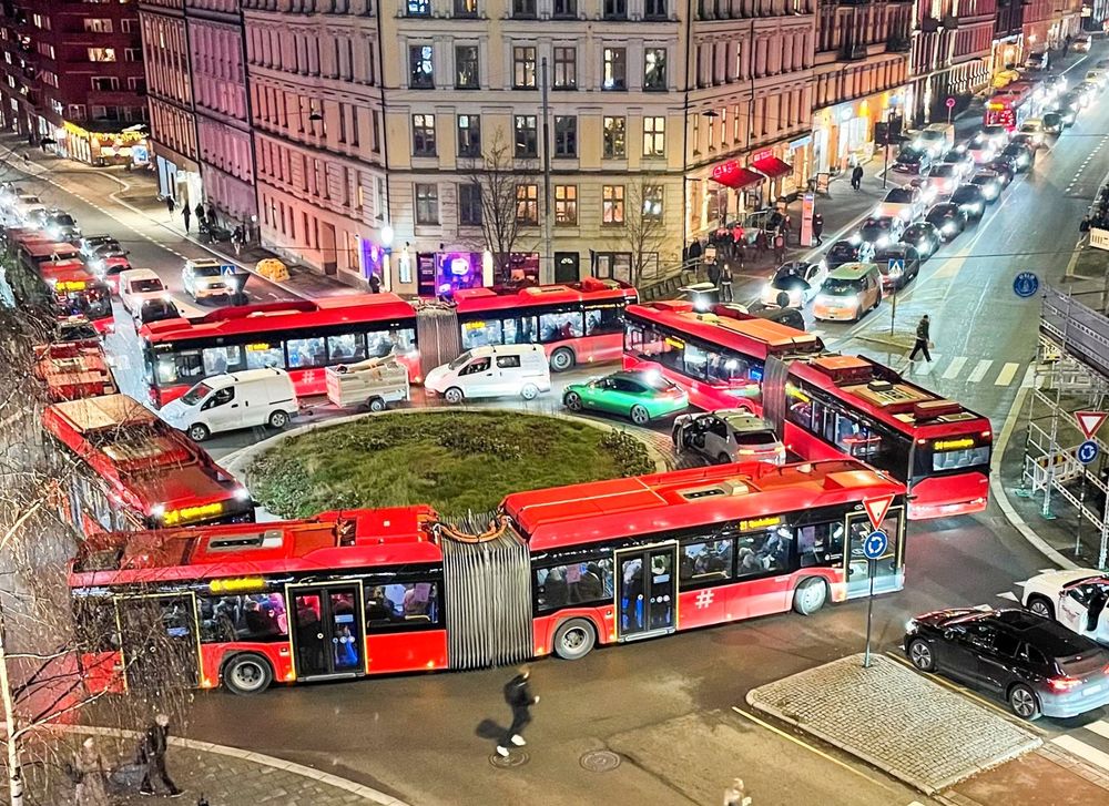 Four Oslo city buses gridlock themselves on a roundabout, with cars contained inside the ring of buses.