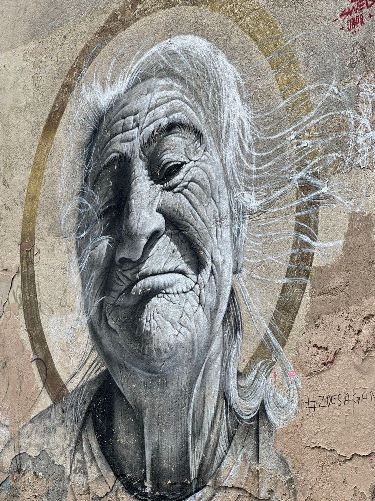 Wall art of older women painted on retaining wall.