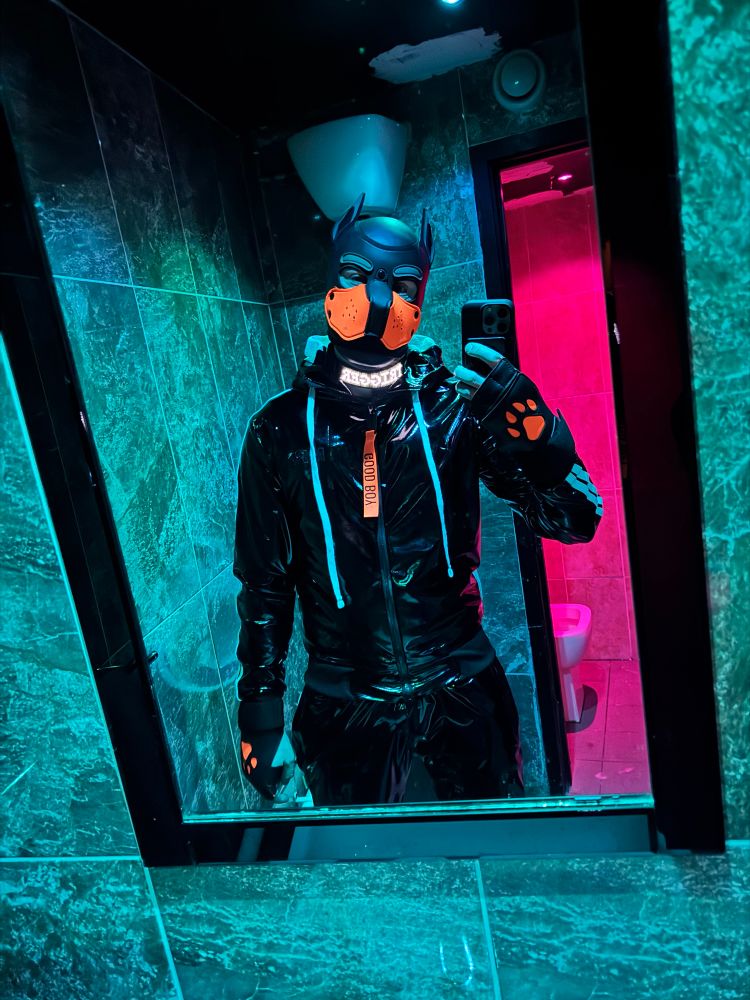 Me in a mirror with my PVC tracksuit on and my light up LED collar saying “Trigger”