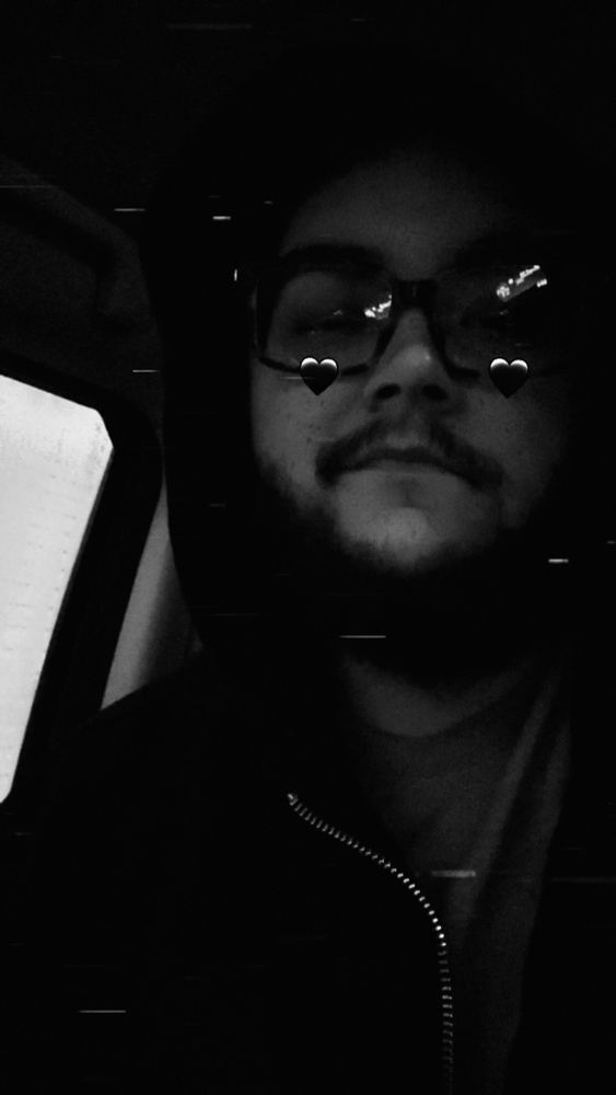 Black and white photo of man in black zip up hoodie, Snapchat filter of black hearts on cheeks 