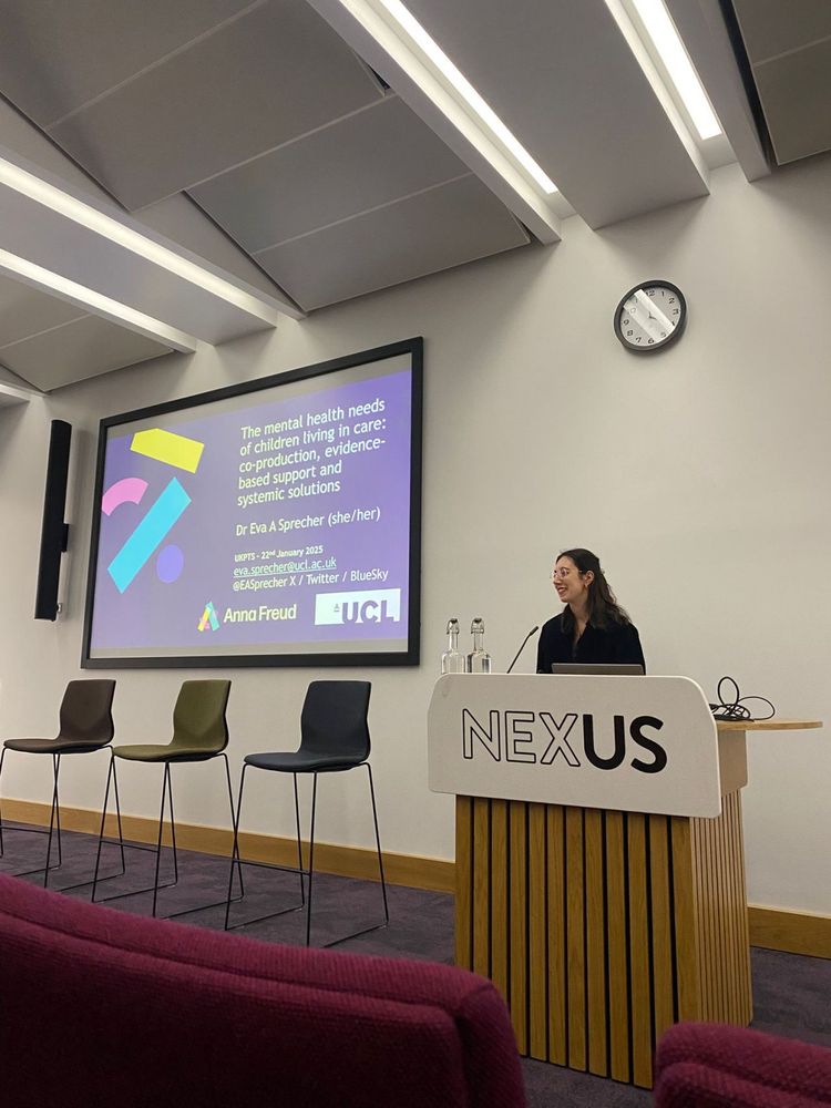 Eva stands at a podium in front of a screen that reads 'The mental health needs of children living in care; coproduction, evidence-based support and systemic solutions'