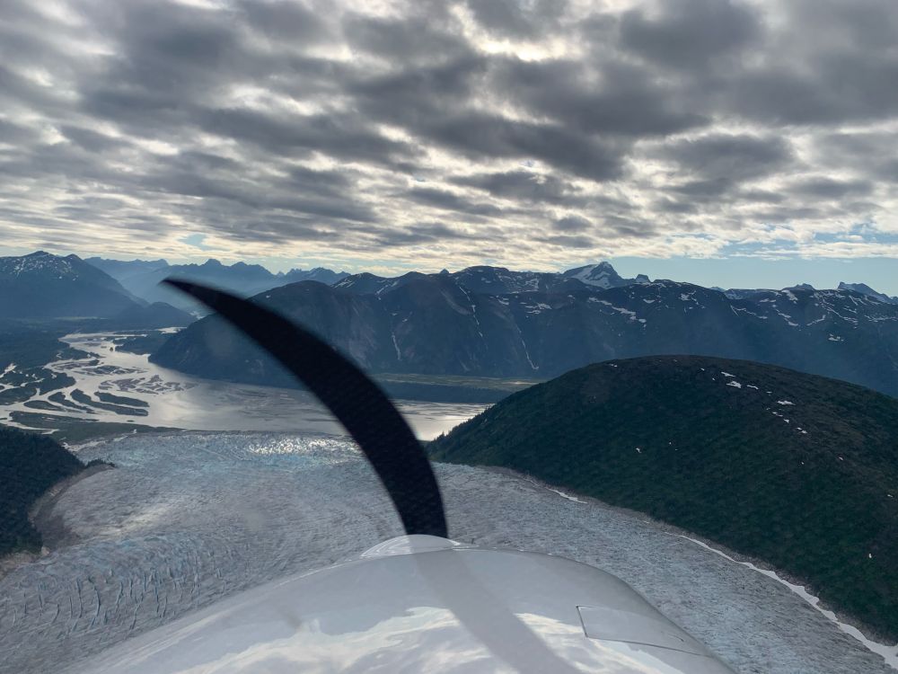 View of Taku Glacier (I think?) terminating in Taku Inlet, with mountains and gray clouds in the background. 