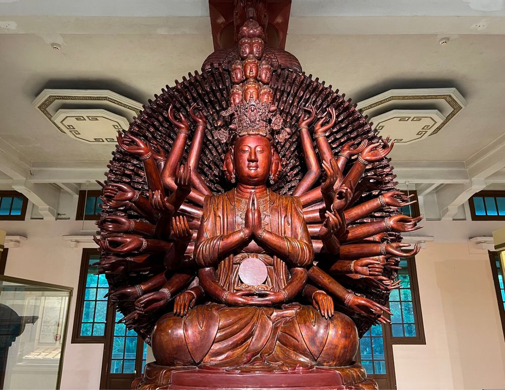 Large painted red wooden statue of seated bodhisattva with many arms and heads